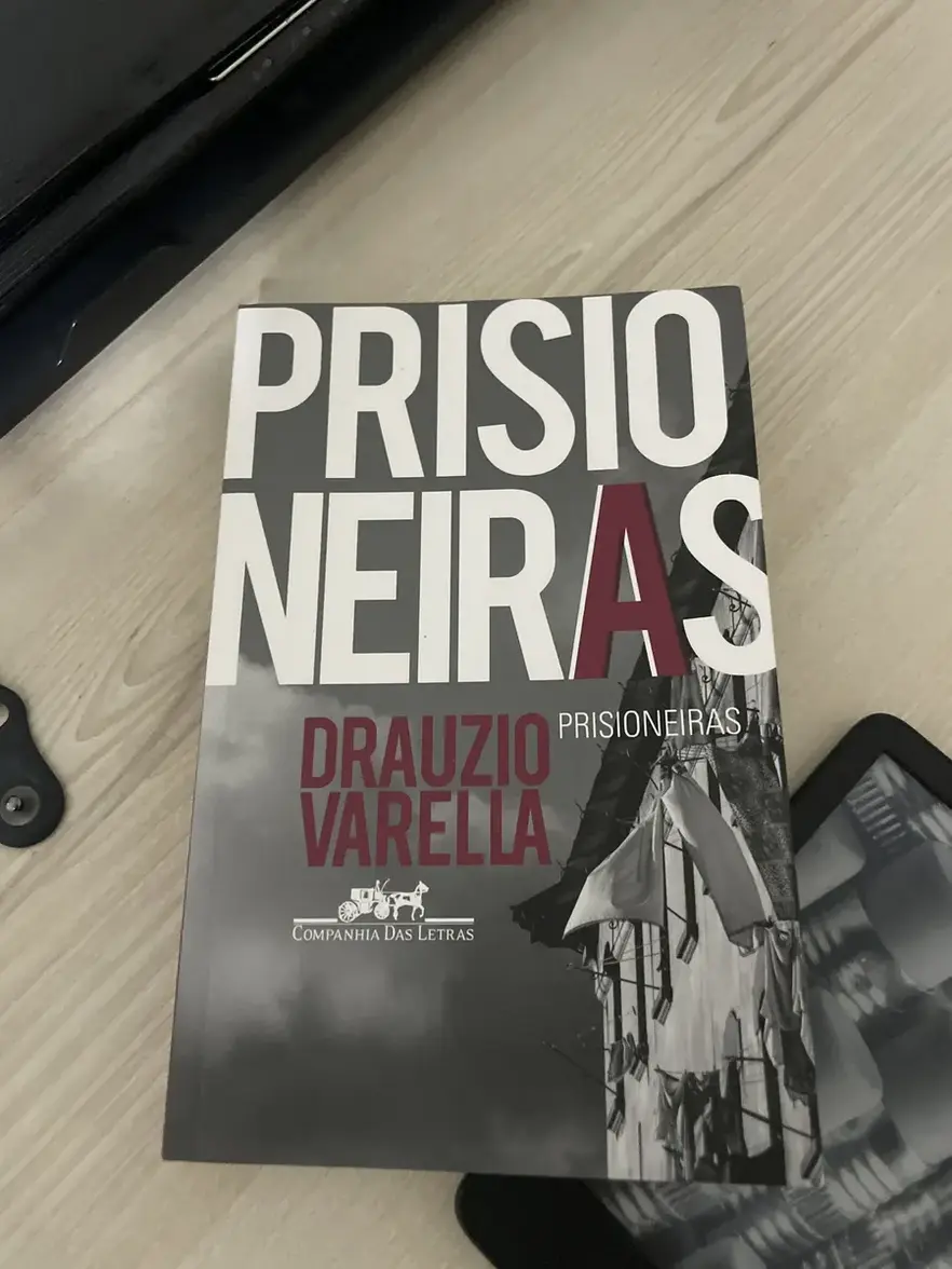 Livro Prisioneiras de Drauzio Varella aberto sobre uma mesa com óculos de leitura